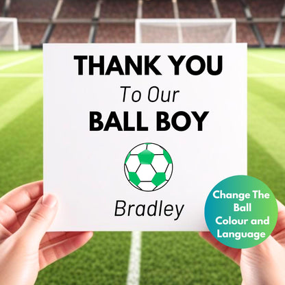 A person is holding a white thank you card in front of a background of a soccer field. The card says "Thank You to Our Ball Boy" with a green and white soccer ball graphic and the name "Bradley" as an example of a personalized name. There's a note indicating that customers can change the ball color and language.