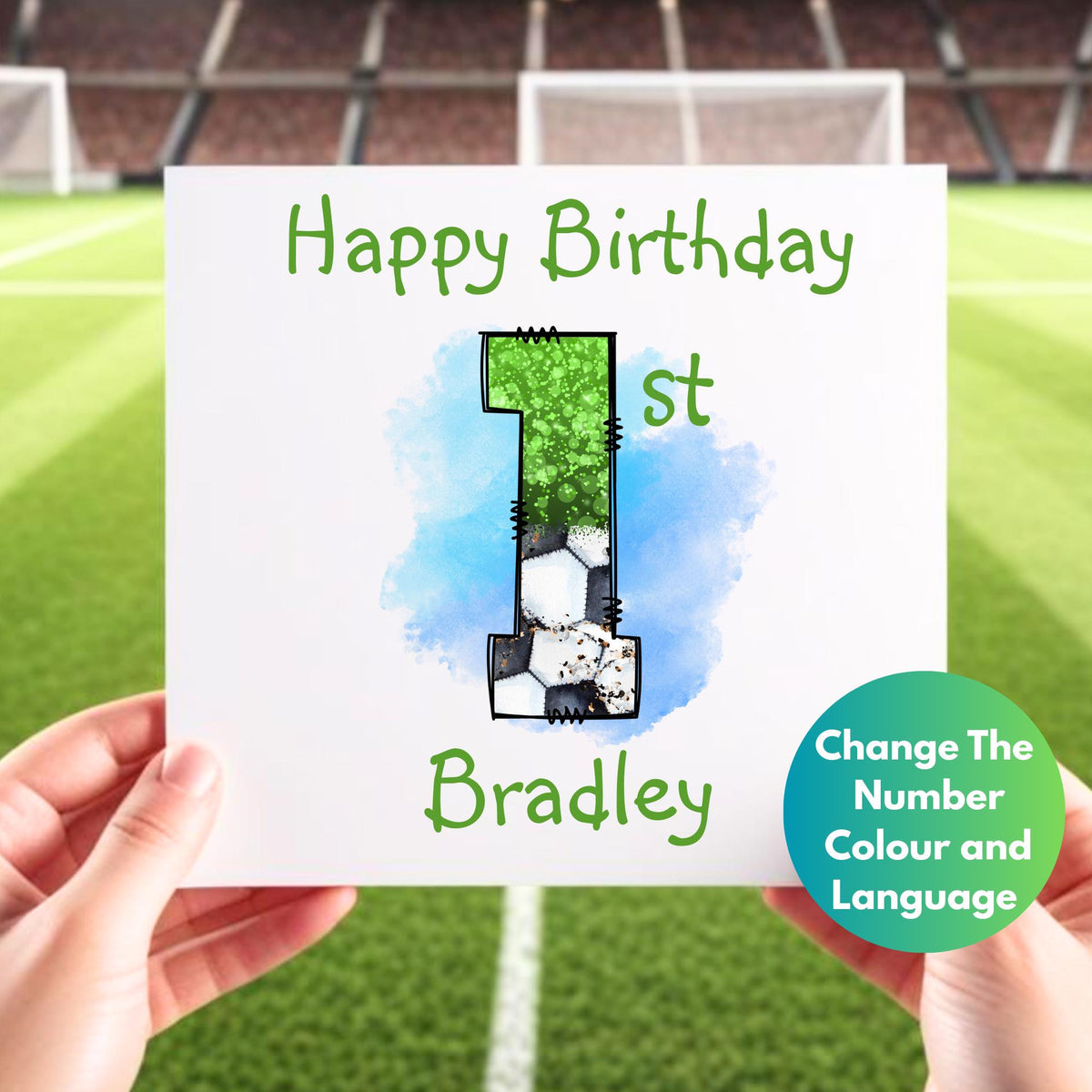Close-up studio shot of a person holding a square, white 1st birthday card with a football theme, reading "Happy Birthday" in green letters, the number "1st" filled with a mix of green and football pattern, above the name "Bradley" also in green, with the background of the photo being a blurry football field and stadium.