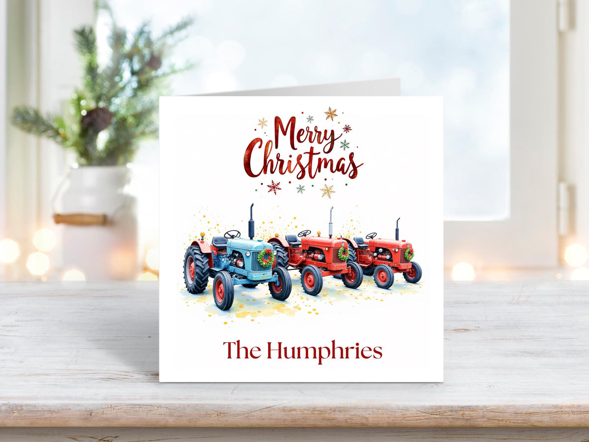 Christmas card featuring three vintage tractors decorated with festive wreaths, including two red and one blue model, with the text “Merry Christmas” above and personalised family name “The Humphries” below.