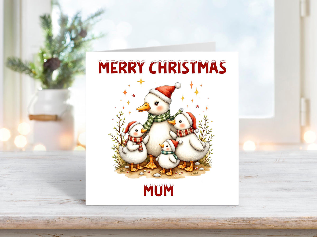 Christmas card featuring a family of ducks in Santa hats and scarves, surrounded by festive tree branches and sparkles, with “Merry Christmas Mum” in red text.