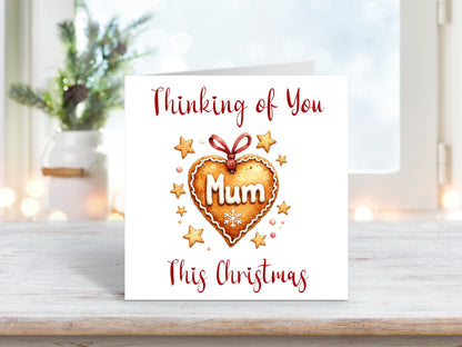 Christmas card featuring a heart-shaped gingerbread cookie with the word “Mum” iced in white, surrounded by gold stars and the words “Thinking of You This Christmas.”