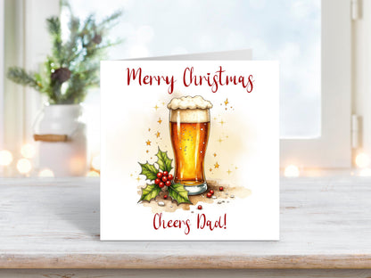 Christmas card featuring a pint of beer with a frothy head, surrounded by holly leaves and red berries, with the words “Merry Christmas Cheers Dad.”