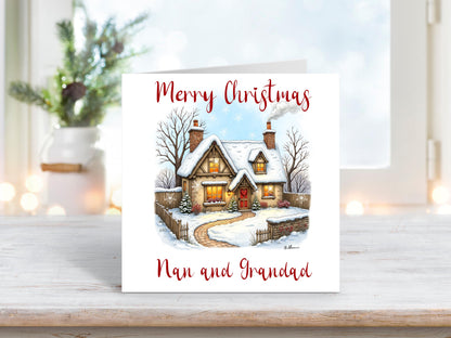 Christmas card featuring a cosy snow-covered cottage with a red door, glowing windows, and a smoking chimney, with the words “Merry Christmas Nan and Grandad” on a white background.