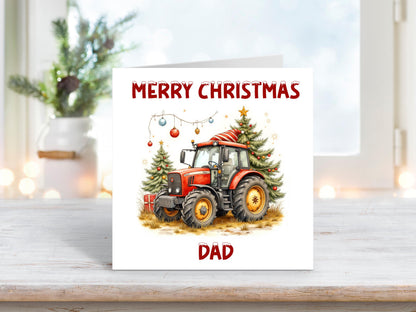 Personalised Christmas card featuring a red tractor wearing a Santa hat, parked beside two decorated Christmas trees with baubles, and the text “Merry Christmas Dad” in festive red lettering.