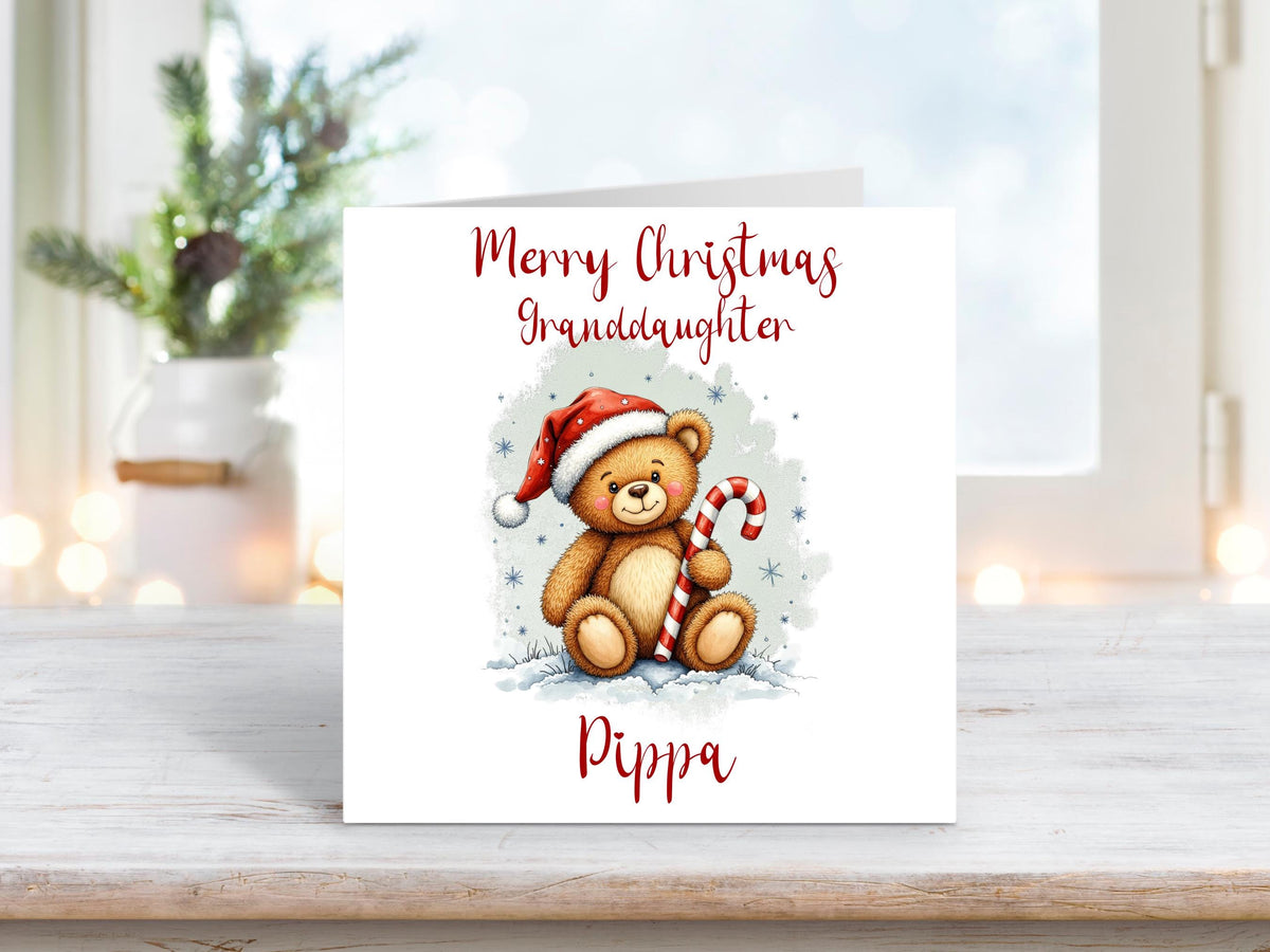 Christmas card for a granddaughter featuring a cute teddy bear in a Santa hat holding a candy cane, with a personalised name underneath.