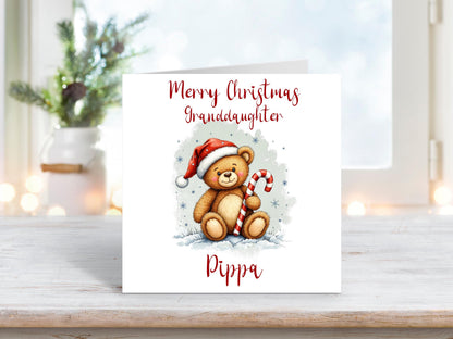 Christmas card for a granddaughter featuring a cute teddy bear in a Santa hat holding a candy cane, with a personalised name underneath.