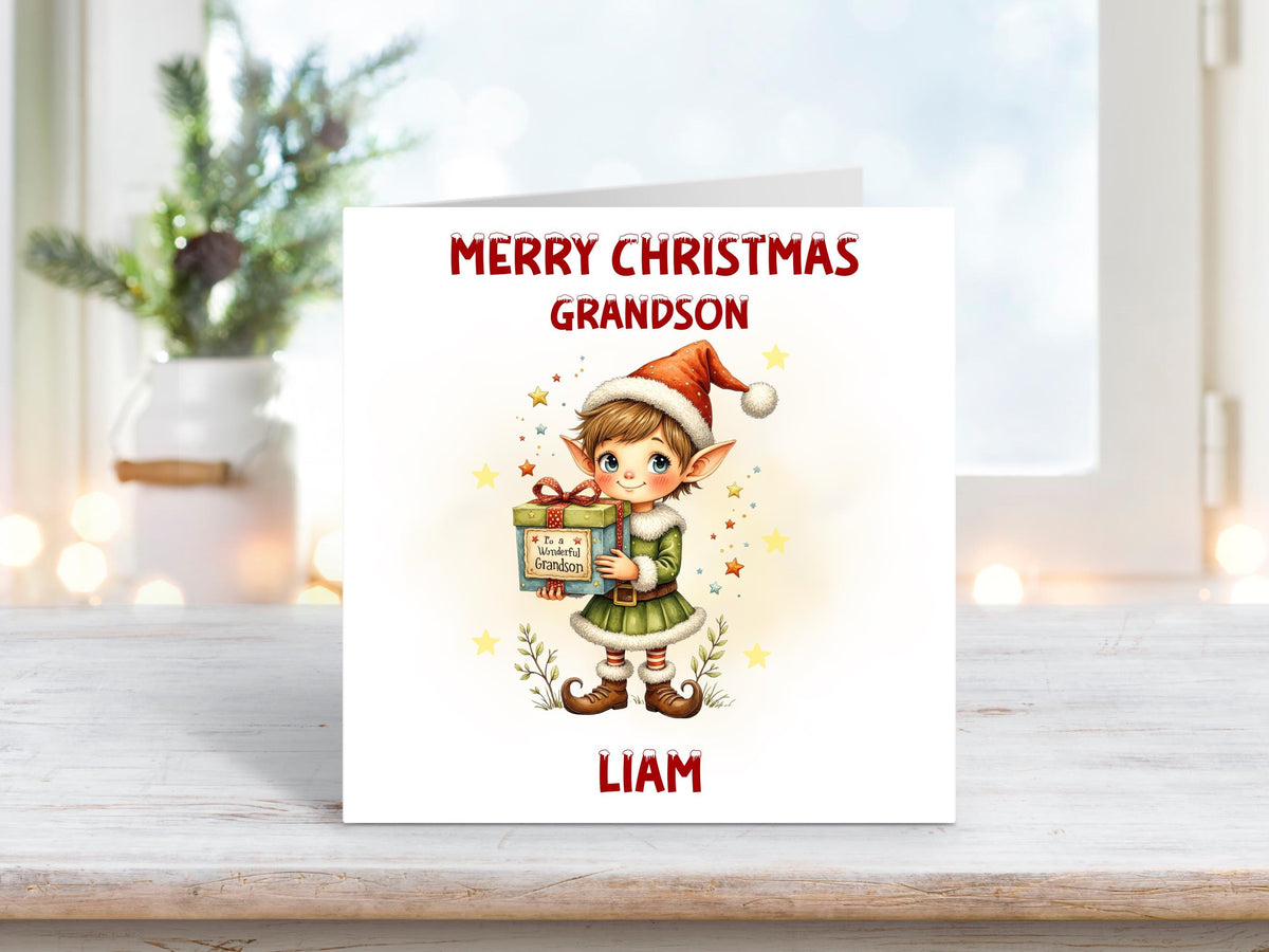 Christmas card for grandson featuring a festive elf in a green outfit and red hat holding a wrapped gift with “To A Wonderful Grandson” on the tag.