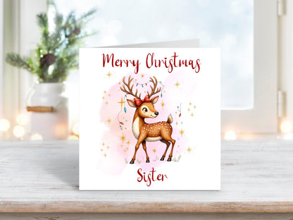 Christmas card for sister featuring a graceful reindeer with antlers decorated with fairy lights, set against a soft pink background with gold stars.