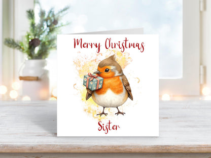 Christmas card for sister featuring a sweet robin holding a green gift on a soft yellow and orange background.