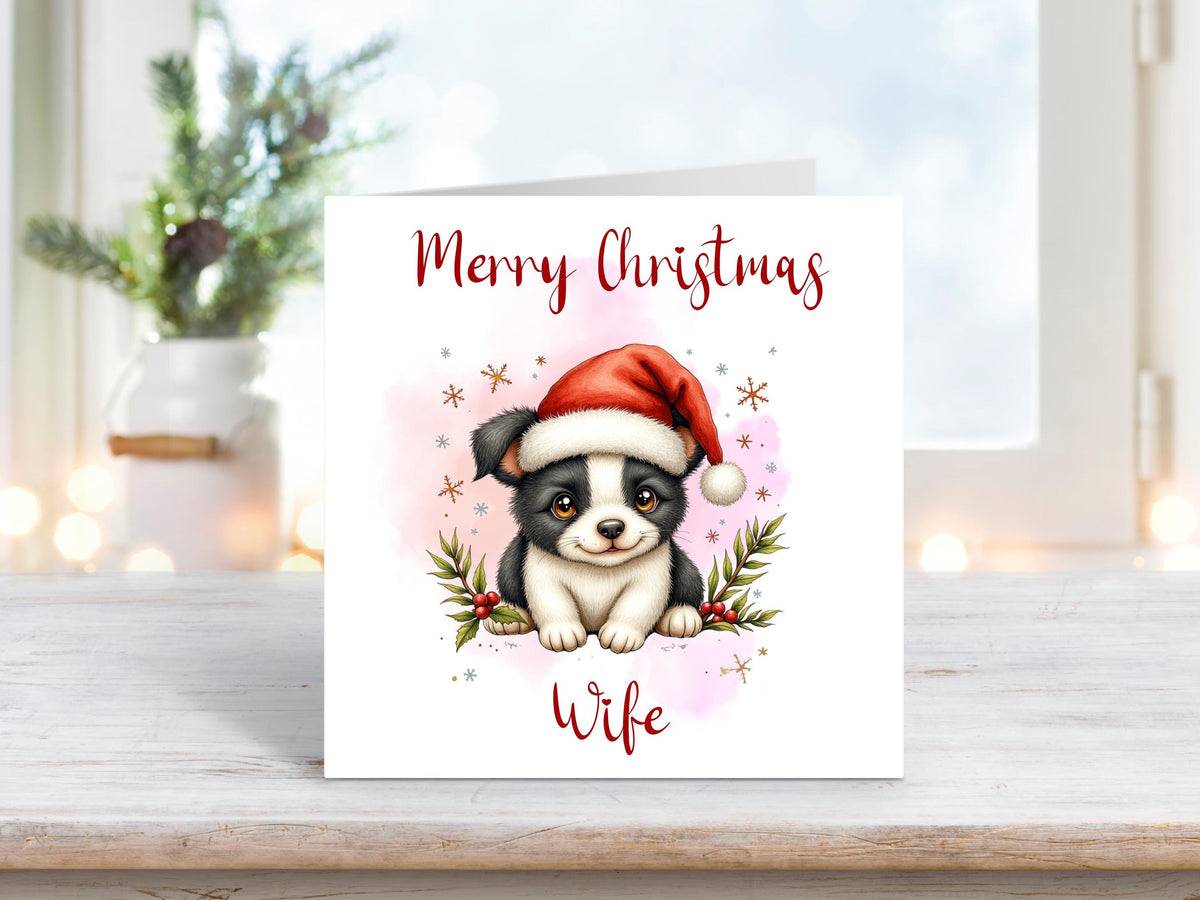 Christmas card for wife featuring a sweet black and white puppy wearing a Santa hat, with holly and snowflakes.