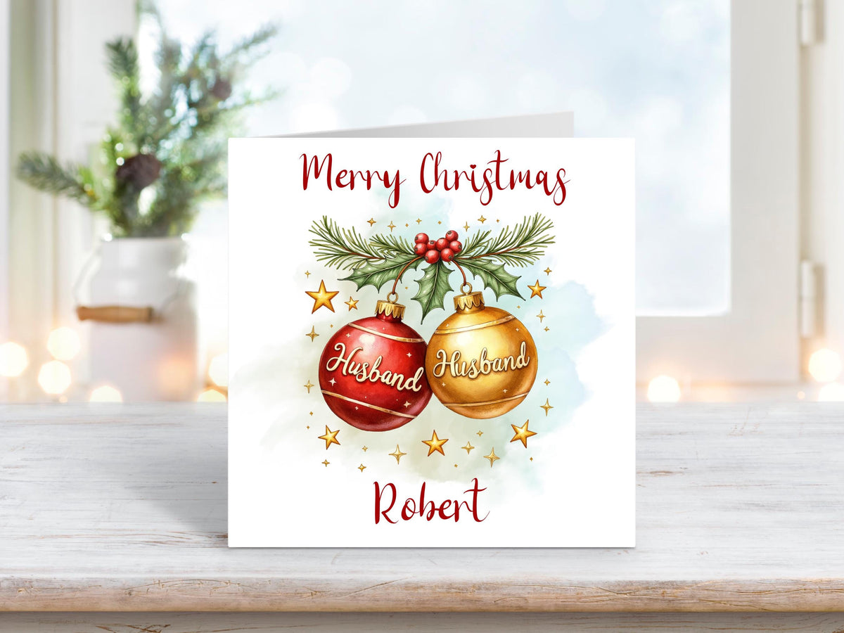 Christmas card for husband with two red and gold baubles labelled “Husband,” decorated with pine, holly, and stars, personalised with name underneath.