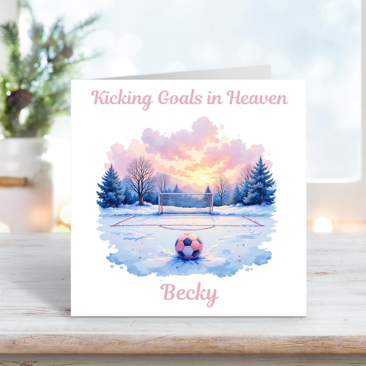 Memorial card showing a pink and purple football resting on a snowy pitch at sunrise, with the text “Kicking Goals in Heaven” and personalised name “Becky.”