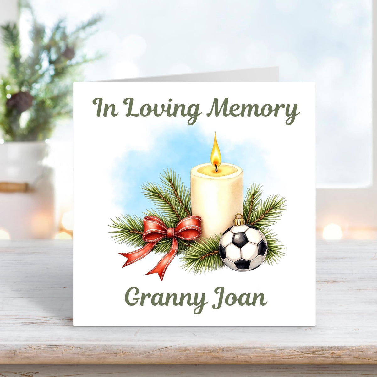 Memorial card with a glowing candle, pine branches, red ribbon, and a small football bauble, with the words “In Loving Memory Granny Joan.”
