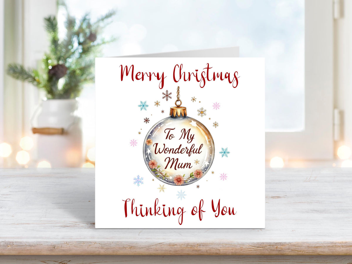 Christmas card featuring a gold bauble with floral detailing and the words “To My Wonderful Mum,” surrounded by snowflakes and stars with text reading “Merry Christmas Thinking of You.”