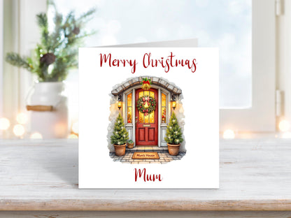 Christmas card featuring a red front door decorated with a wreath and potted Christmas trees, with the words “Merry Christmas Mum” above and below the image.