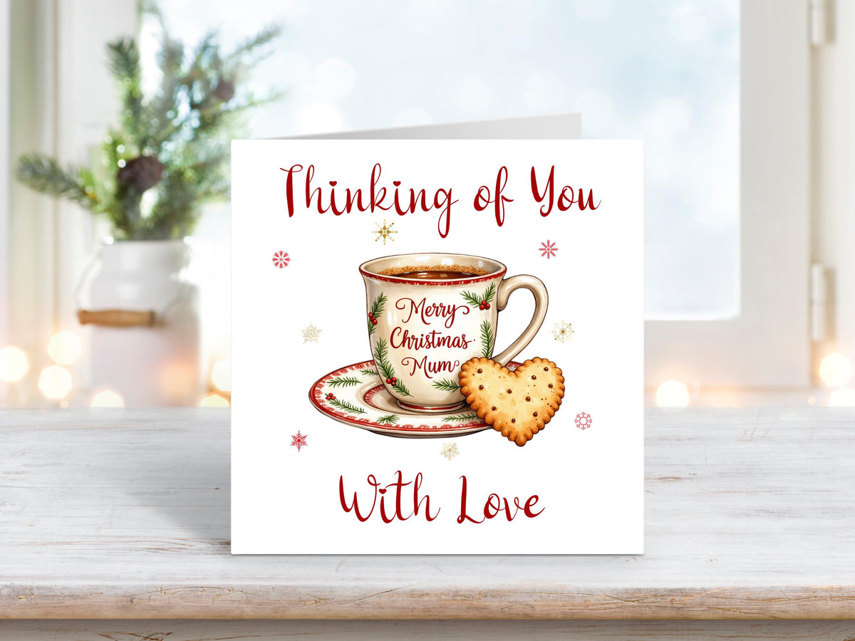 Christmas card featuring a festive teacup and saucer with “Merry Christmas Mum” written on it, and a heart-shaped biscuit beside it, with the words “Thinking of You With Love.”