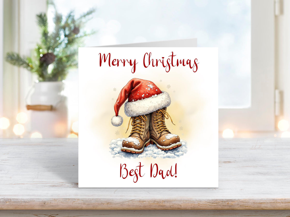 Christmas card featuring a pair of brown boots topped with a red Santa hat, resting in the snow with the words “Merry Christmas Best Dad.”