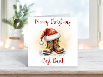 Christmas card featuring a pair of brown boots topped with a red Santa hat, resting in the snow with the words “Merry Christmas Best Dad.”