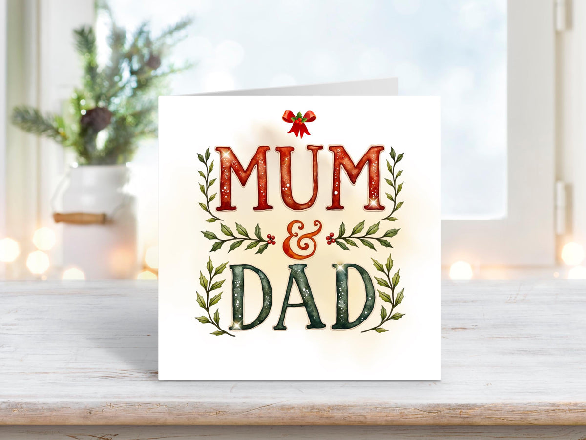 Christmas card featuring bold red and green lettering spelling “Mum & Dad” with holly leaves, berries, and a small red bow on a softly glowing white background.