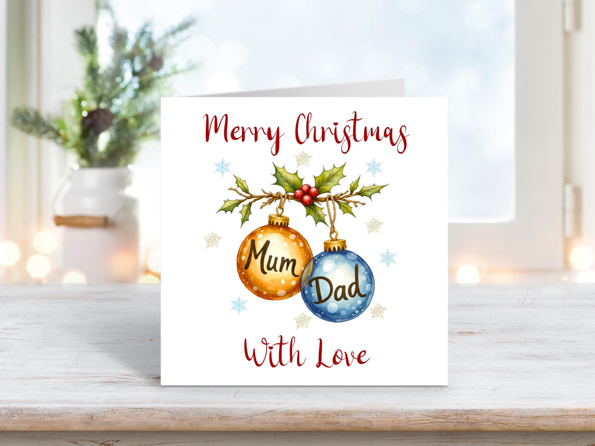 Christmas card featuring two hanging baubles labelled “Mum” and “Dad,” decorated with holly, berries, and snowflakes on a white background, with the words “Merry Christmas With Love.”