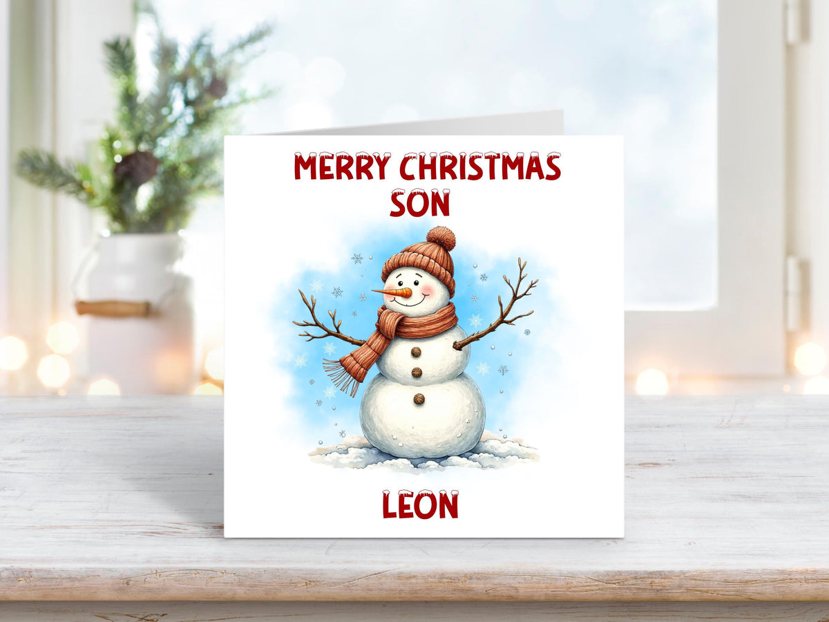 Christmas card featuring a happy snowman wearing a red hat and scarf with stick arms and snowflakes around, set against a blue snowy background, with the words “Merry Christmas Son” and personalised name “Leon.”