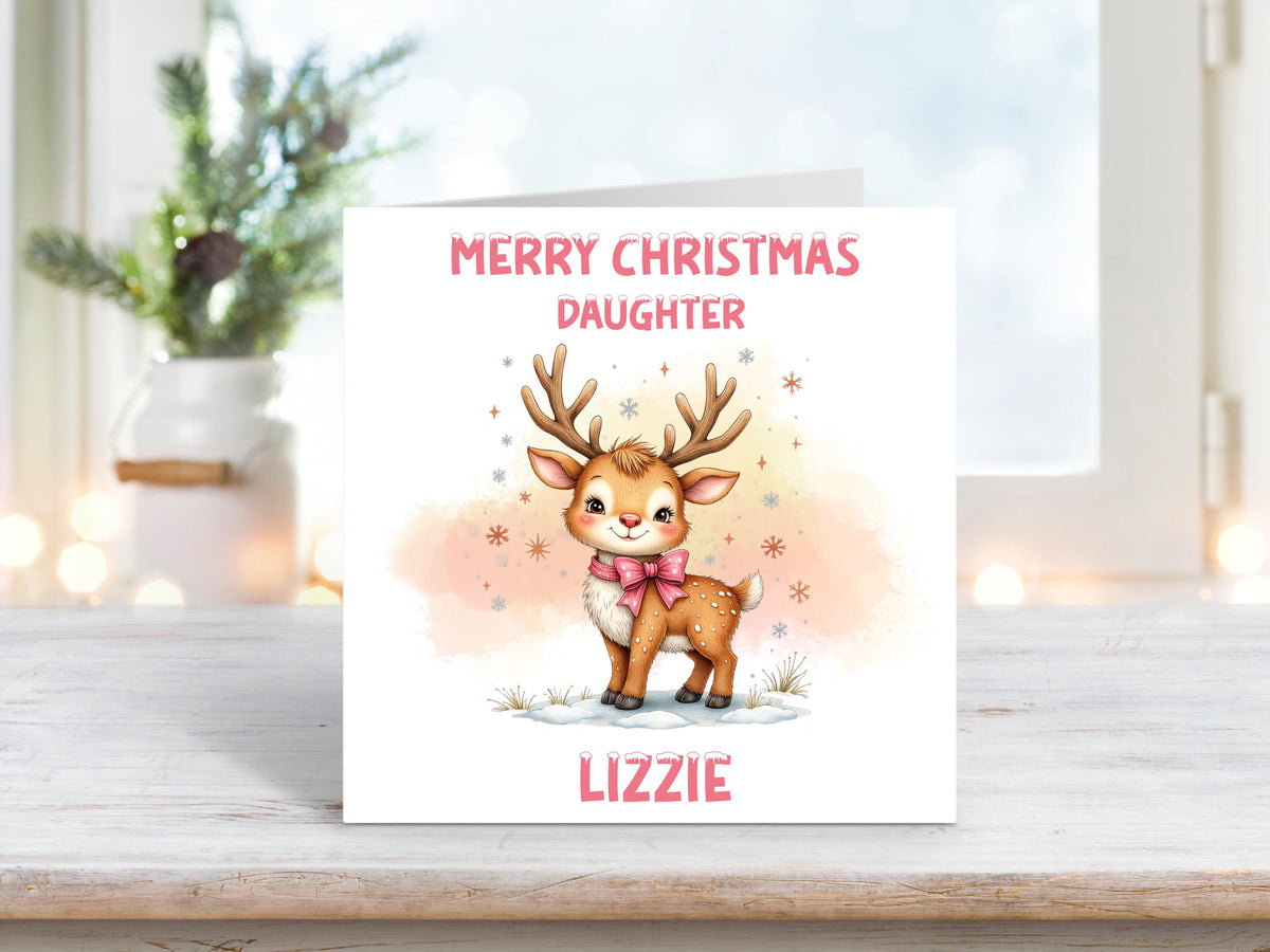 Christmas card featuring an adorable reindeer with a pink bow surrounded by snowflakes and a soft peach background, with the words “Merry Christmas Daughter” and personalised name “Lizzie.”