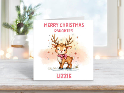 Christmas card featuring an adorable reindeer with a pink bow surrounded by snowflakes and a soft peach background, with the words “Merry Christmas Daughter” and personalised name “Lizzie.”
