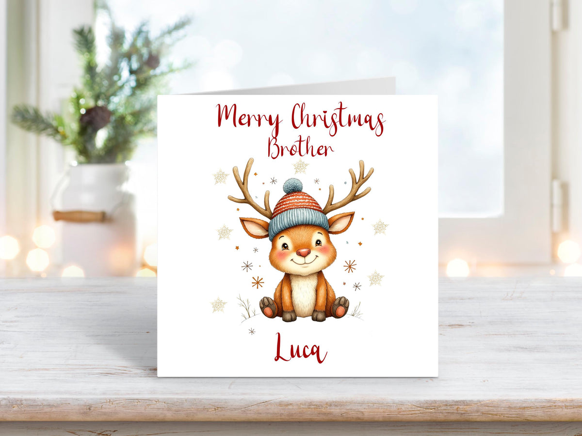 Cute cartoon-style Christmas card featuring a smiling reindeer in a woolly hat, surrounded by snowflakes. Text reads “Merry Christmas Brother” with personalisation for “Luca”.