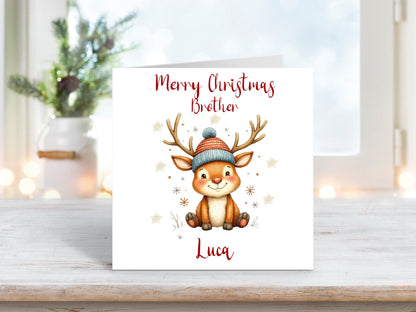 Cute cartoon-style Christmas card featuring a smiling reindeer in a woolly hat, surrounded by snowflakes. Text reads “Merry Christmas Brother” with personalisation for “Luca”.