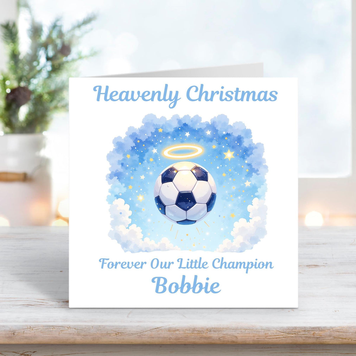 Memorial Christmas card with a football floating in the clouds surrounded by stars and a glowing halo, with the words “Heavenly Christmas Forever Our Little Champion Bobbie.”