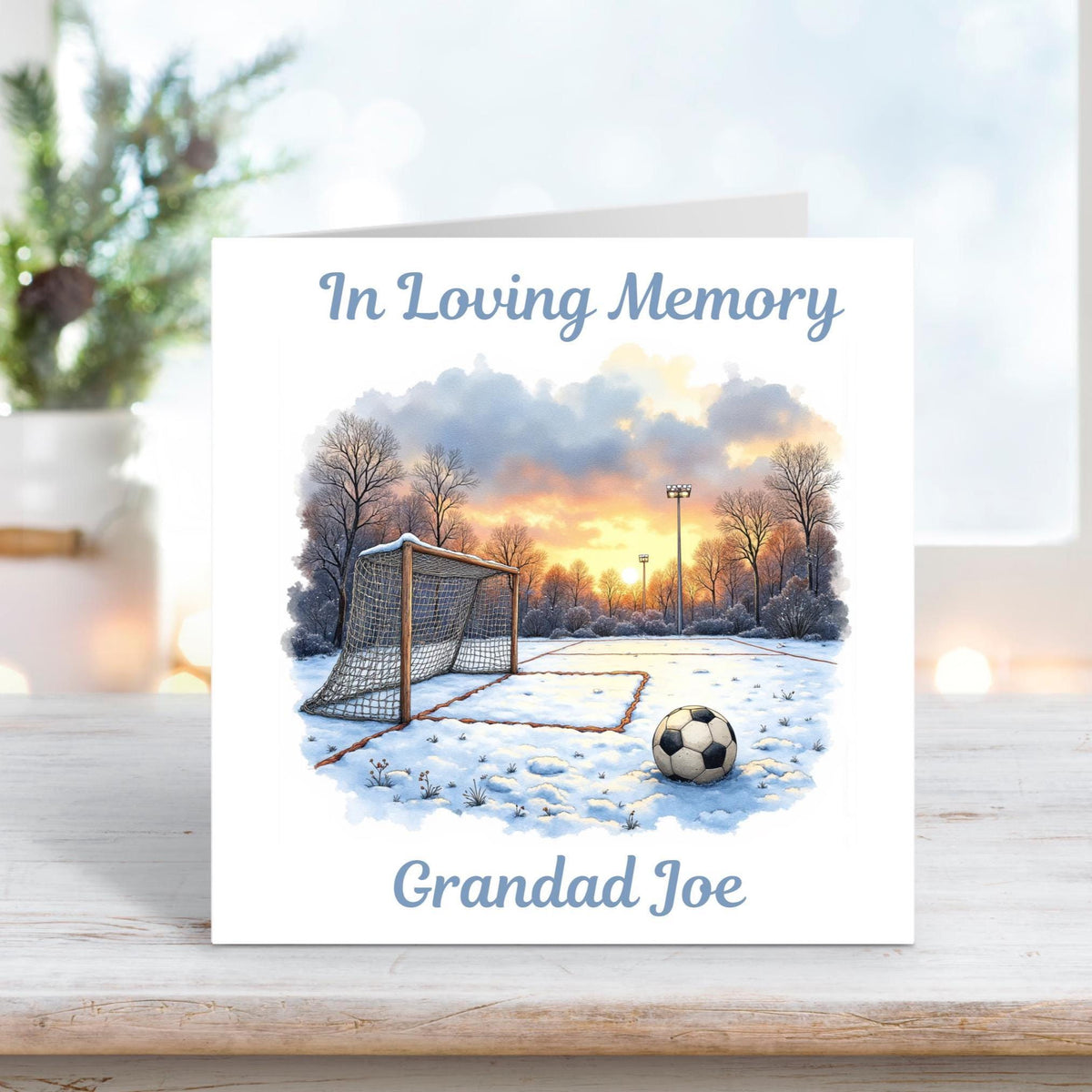 Memorial card featuring a football resting on a snowy pitch at sunrise, with the text “In Loving Memory” and personalised name “Grandad Joe.”