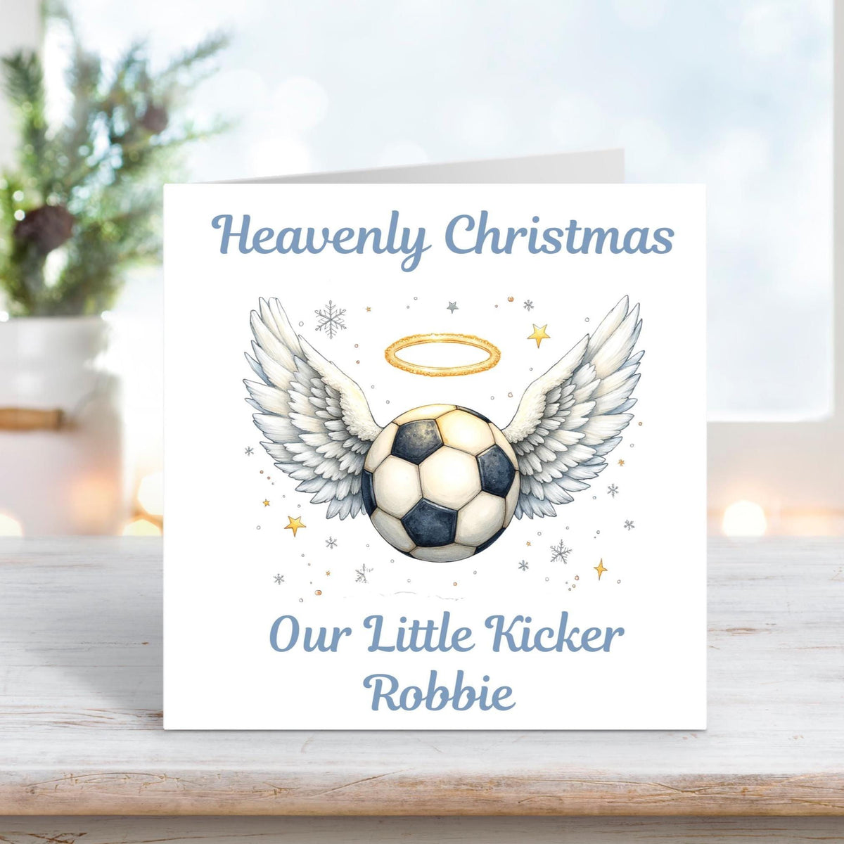 Memorial Christmas card featuring a football with angel wings and halo, surrounded by golden stars and snowflakes, with the words “Heavenly Christmas Our Little Kicker Robbie.”
