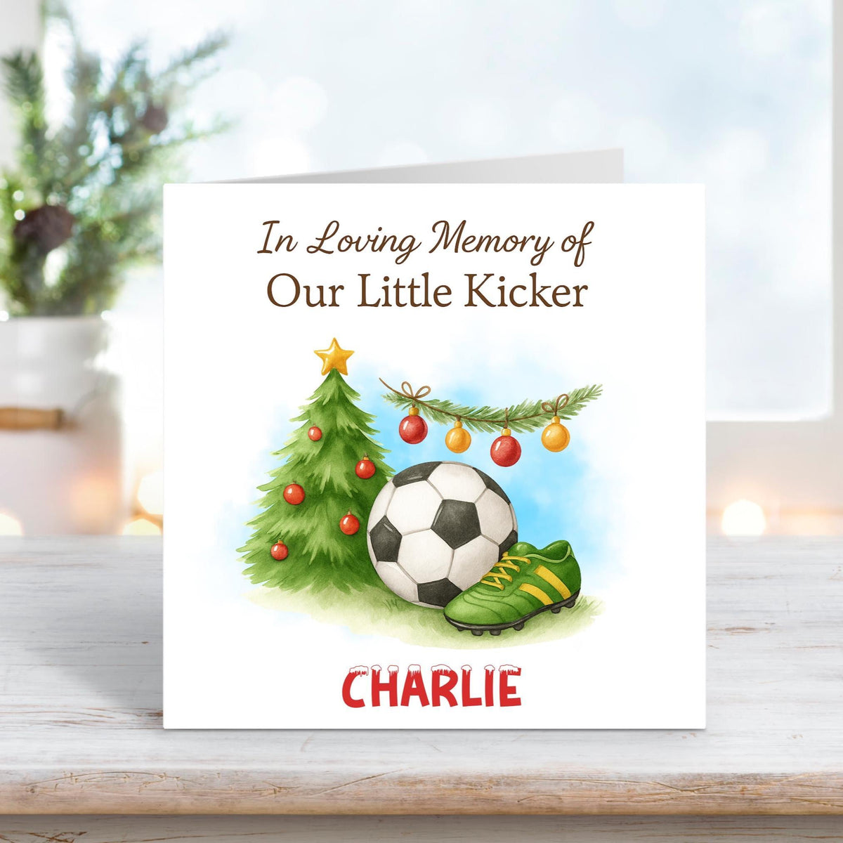 Memorial Christmas card showing a football, green boots, and a decorated tree under the text “In Loving Memory of Our Little Kicker,” personalised with the name Charlie.