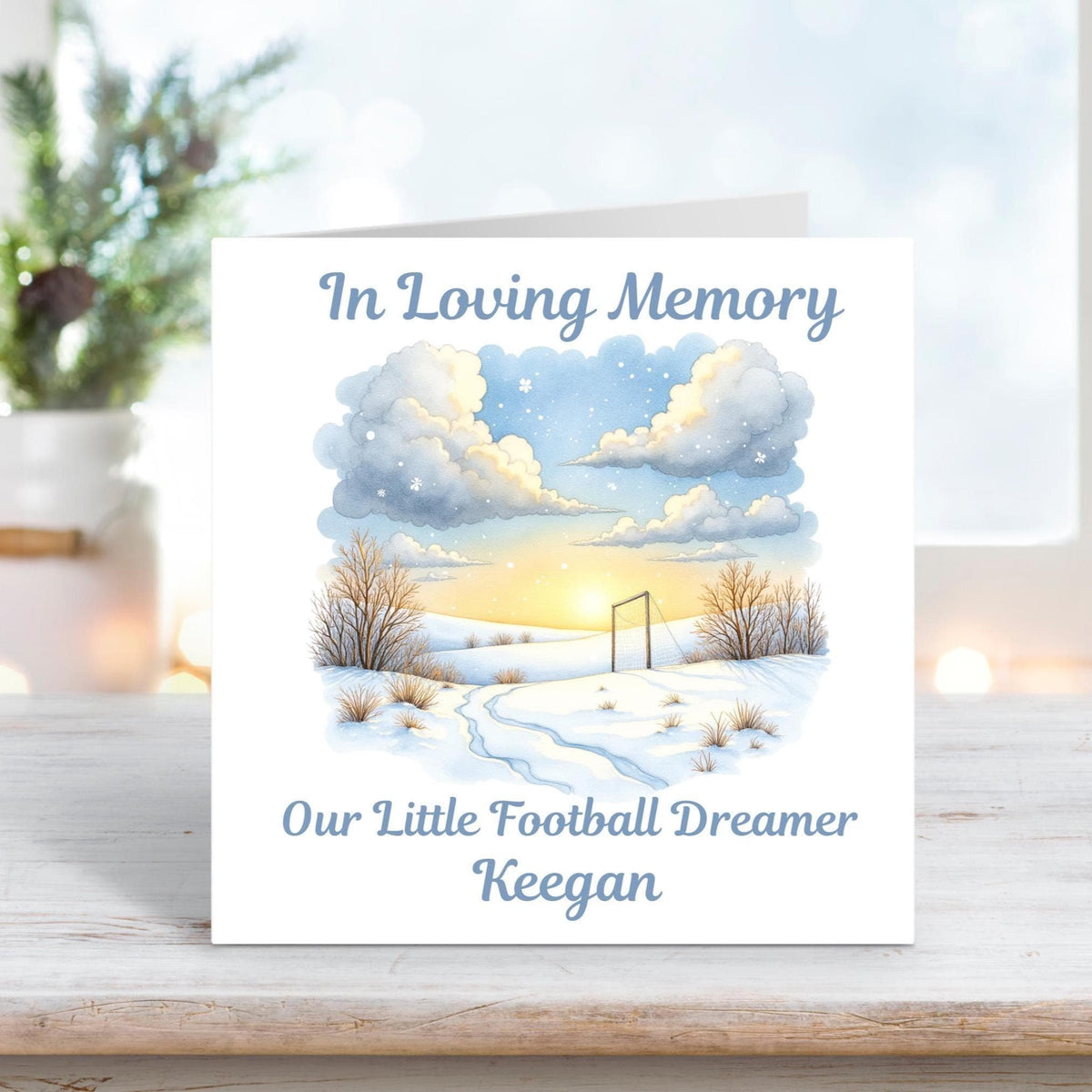 Memorial card featuring a peaceful snowy football field at sunset with the words “In Loving Memory – Our Little Football Dreamer Keegan.”