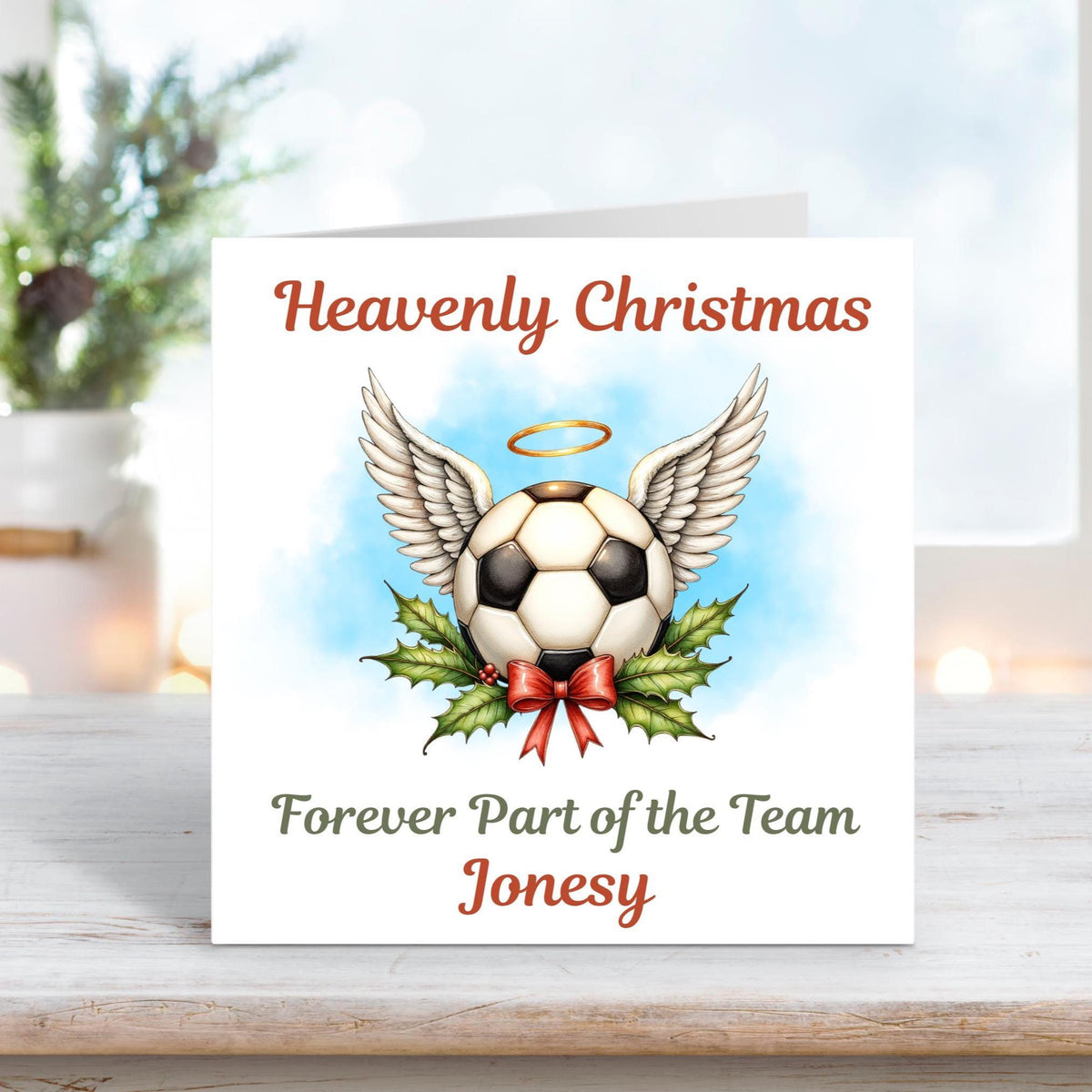 Memorial Christmas card showing a football with angel wings and a golden halo above holly and ribbon, with the words “Heavenly Christmas – Forever Part of the Team Jonesy.”