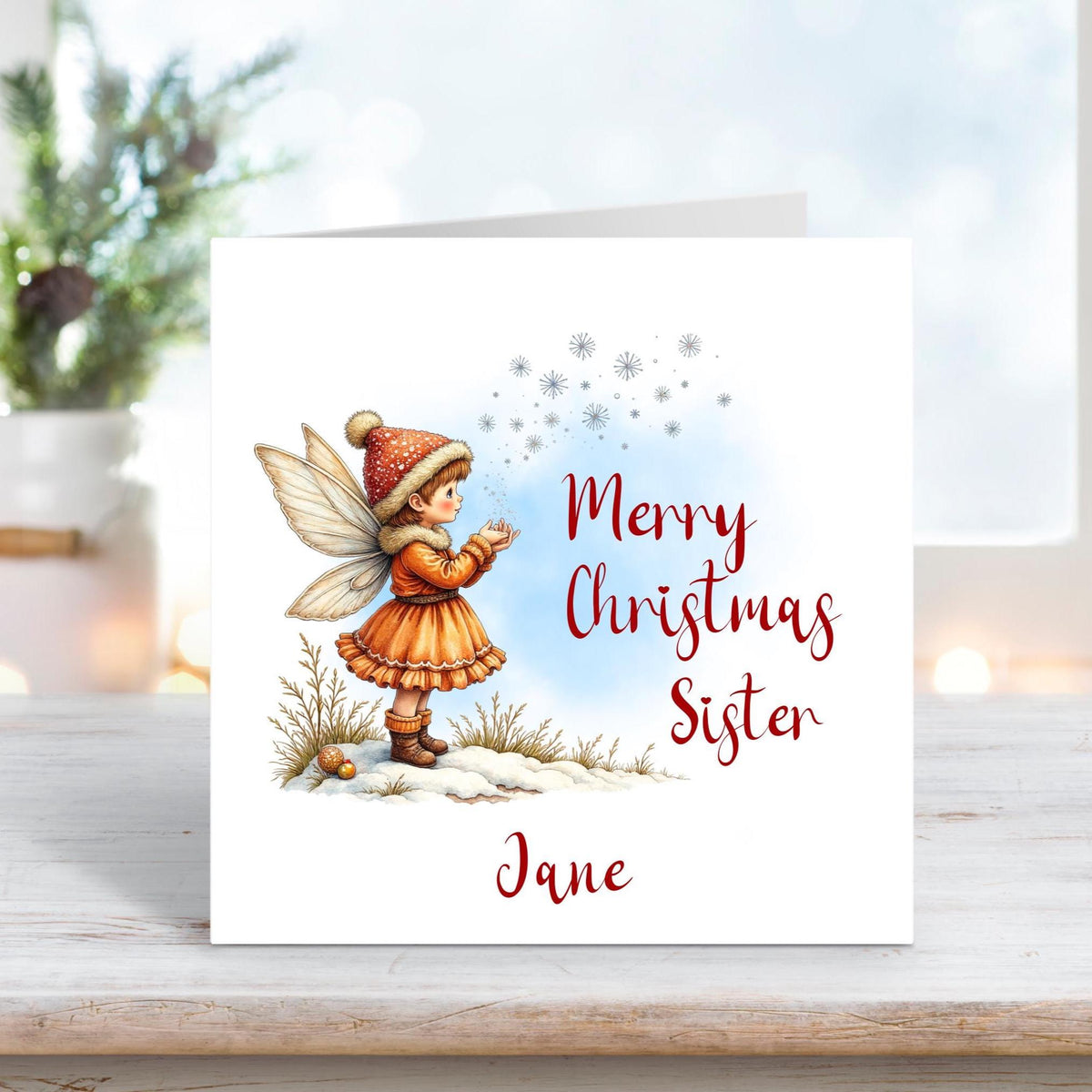 Christmas card for sister with a fairy girl in an orange dress and hat blowing snowflakes on a snowy background.