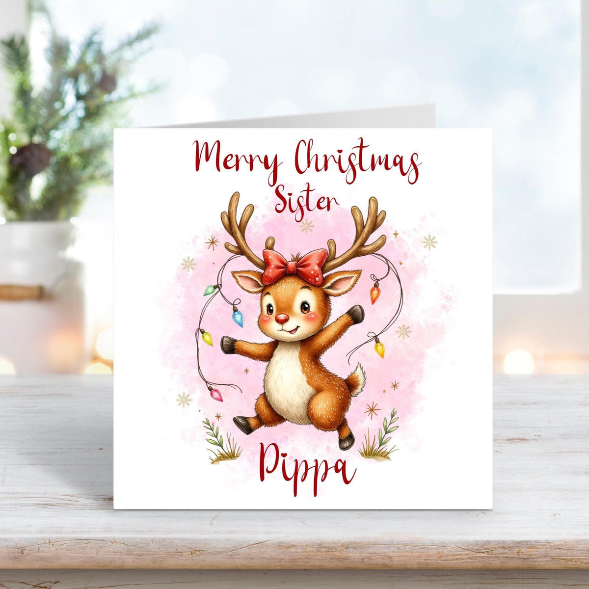 Christmas card for sister featuring a cute reindeer with a red bow and fairy lights wrapped around its antlers on a pink snowy background.