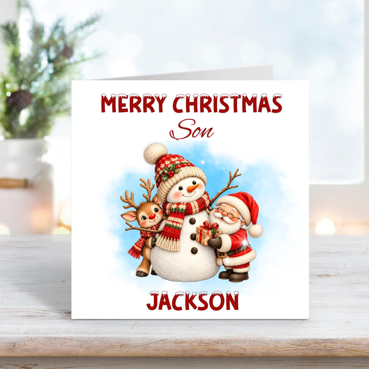 Personalised Merry Christmas Son card featuring a cheerful snowman wearing a festive knitted hat and scarf, alongside a cute reindeer and Santa Claus holding a Christmas present. Snowy blue background with custom name Jackson.
