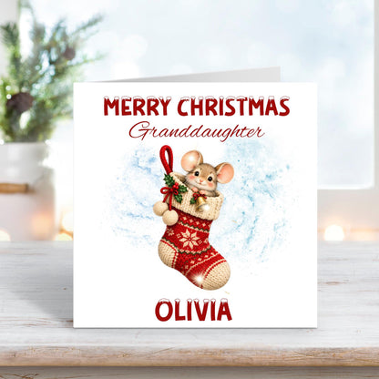 Personalised Merry Christmas Granddaughter card featuring an adorable little mouse peeking out of a red knitted Christmas stocking decorated with snowflakes, holly and bells. Custom name Olivia beneath the festive illustration.