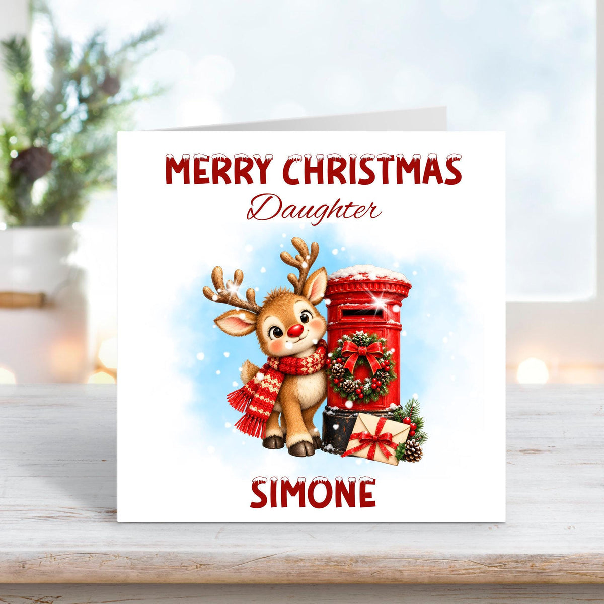Personalised Merry Christmas Daughter card featuring an adorable baby reindeer wearing a red knitted scarf beside a traditional red Christmas postbox decorated with a festive wreath. Snowy blue background, wrapped Christmas present and custom name Simone.
