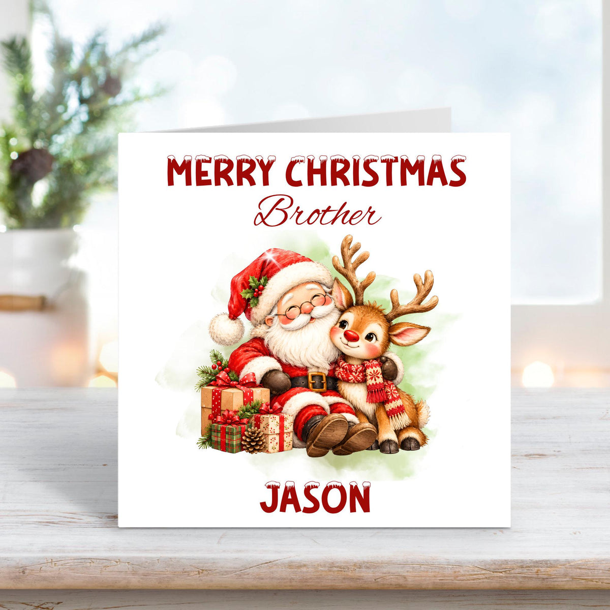 Personalised Merry Christmas Brother card featuring a cheerful Santa Claus cuddling an adorable reindeer wearing a red knitted scarf, surrounded by wrapped Christmas presents, holly and pinecones. Soft green watercolour background with custom name Jason.